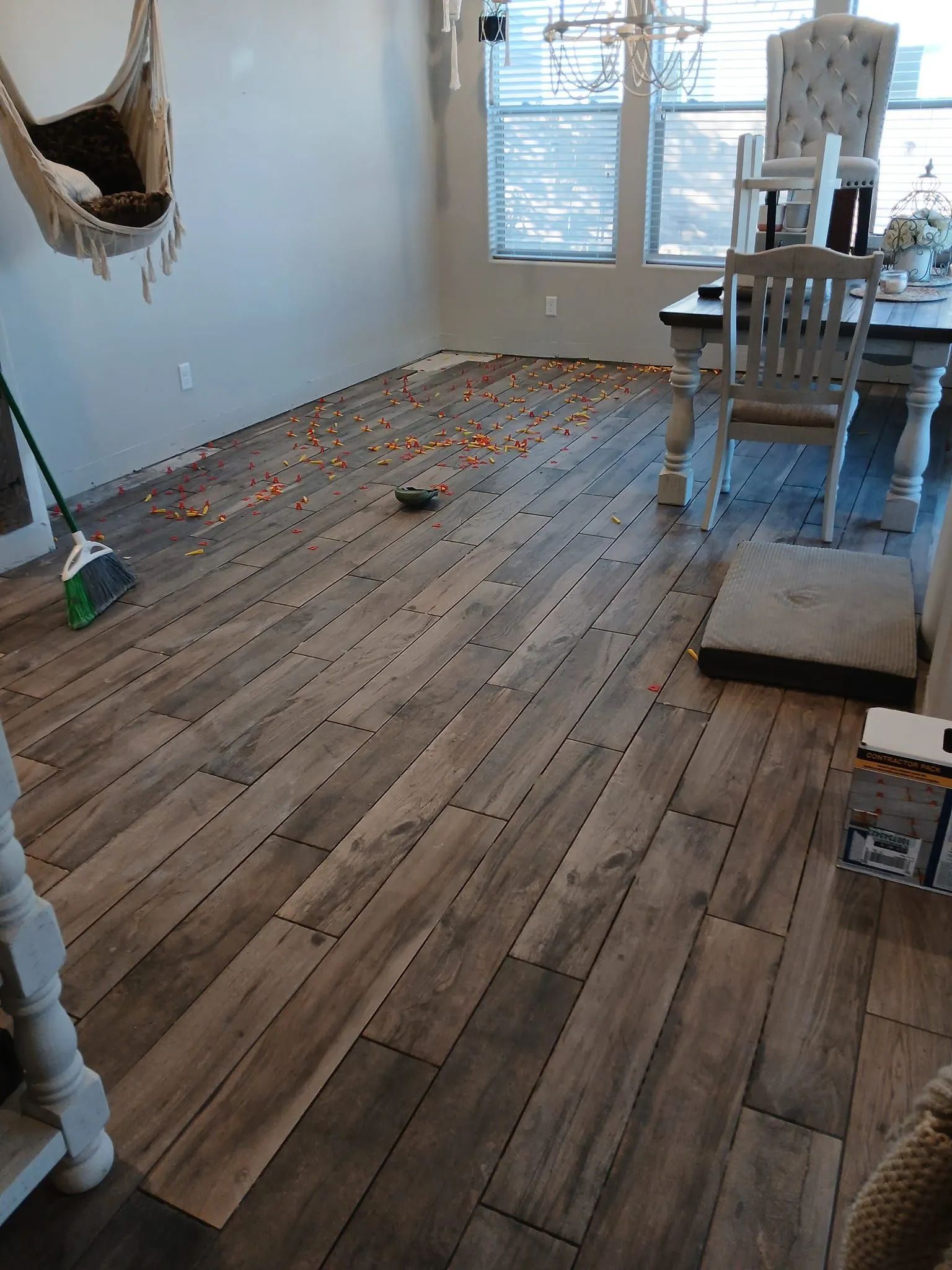 Candy corn scattered on a wooden plank floor in a dining area; broom nearby.