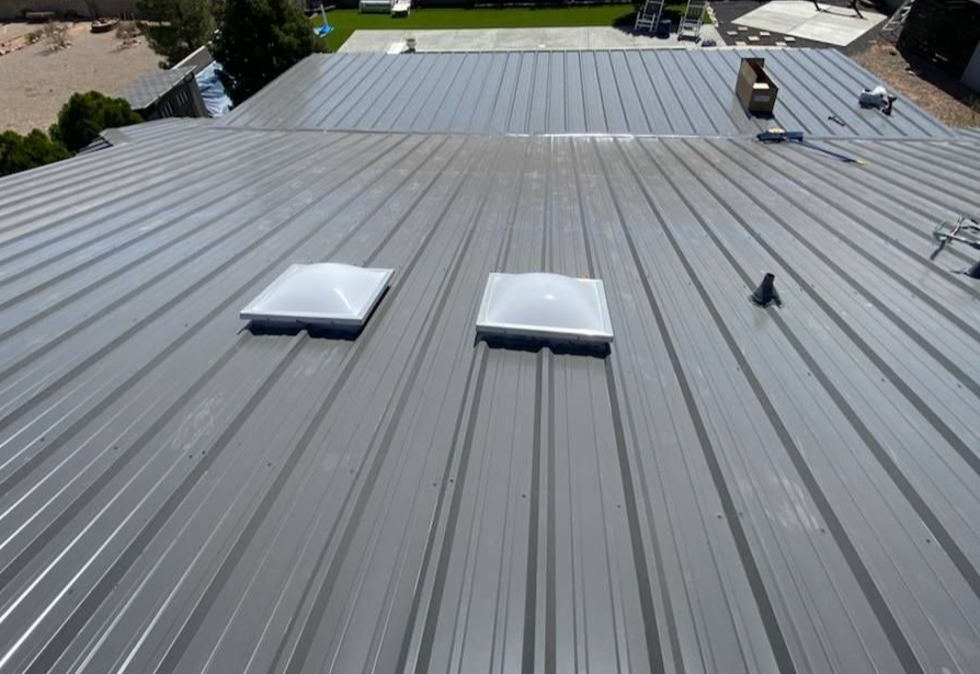 Gray metal roof with two skylights, overlooking a yard.