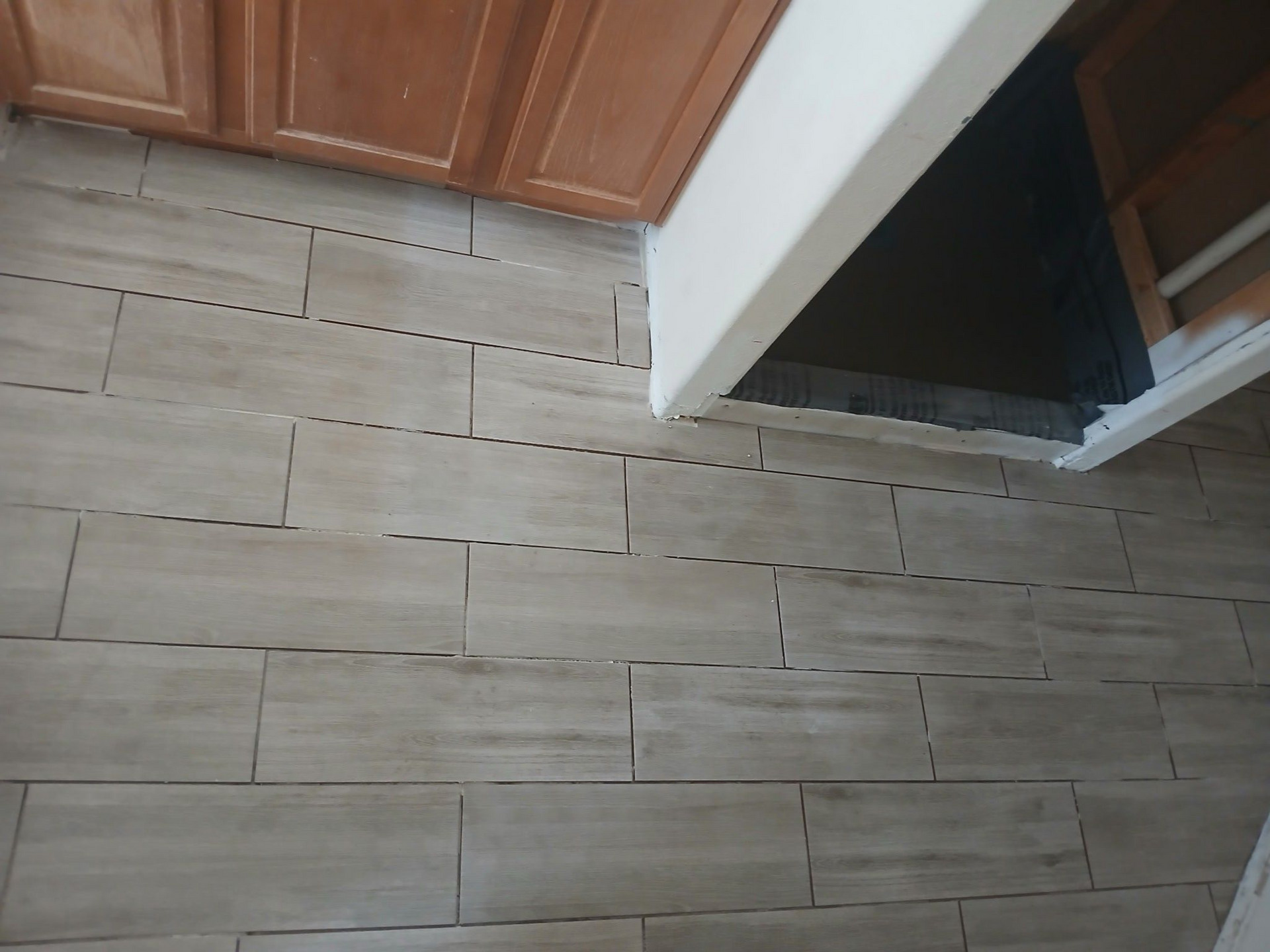 Tiled kitchen floor with tan-colored rectangular tiles under light-brown cabinets and a white-painted opening.