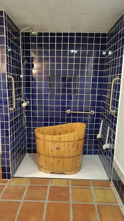 Blue tiled shower with wooden soaking tub, handrails, and a terracotta tiled floor.