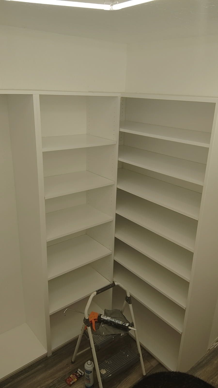 Built-in white shelving unit in a corner. A stepladder is inside the unit.