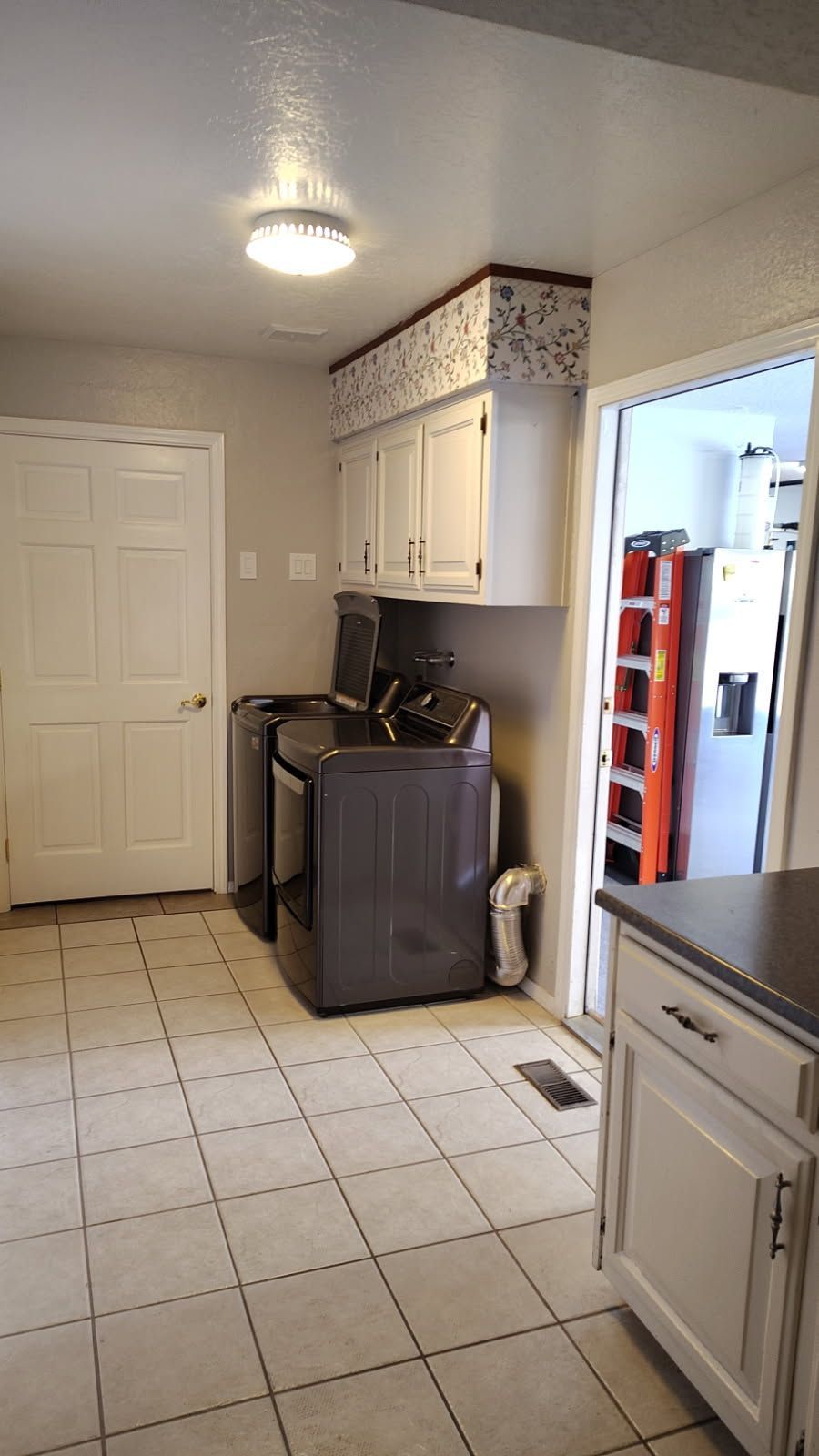 Kitchen with white cabinets, laundry appliances, and a door leading to another room with a red ladder.