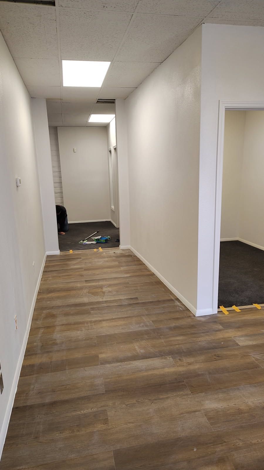 Long hallway with wood-look flooring and white walls, leading to other rooms. Overhead, square lights.