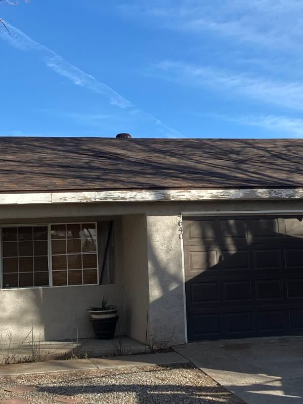 A house exterior with a garage and windows, featuring a brown roof and a blue sky.