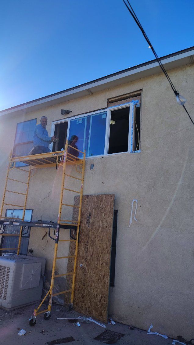 Workers on scaffolding replacing windows on a beige building under a clear blue sky.