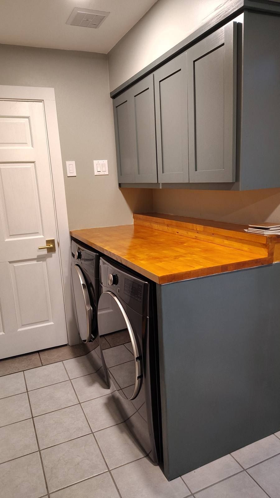 Laundry room with gray cabinets, washer/dryer, and a wood countertop.