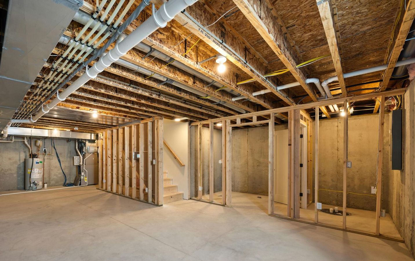 Unfinished basement with exposed wooden framing, plumbing, and concrete walls and floor.