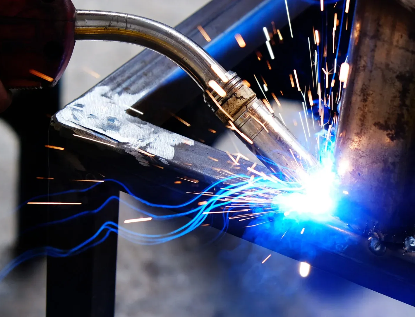 Welder at work, blue sparks from welding torch fusing metal pieces together.