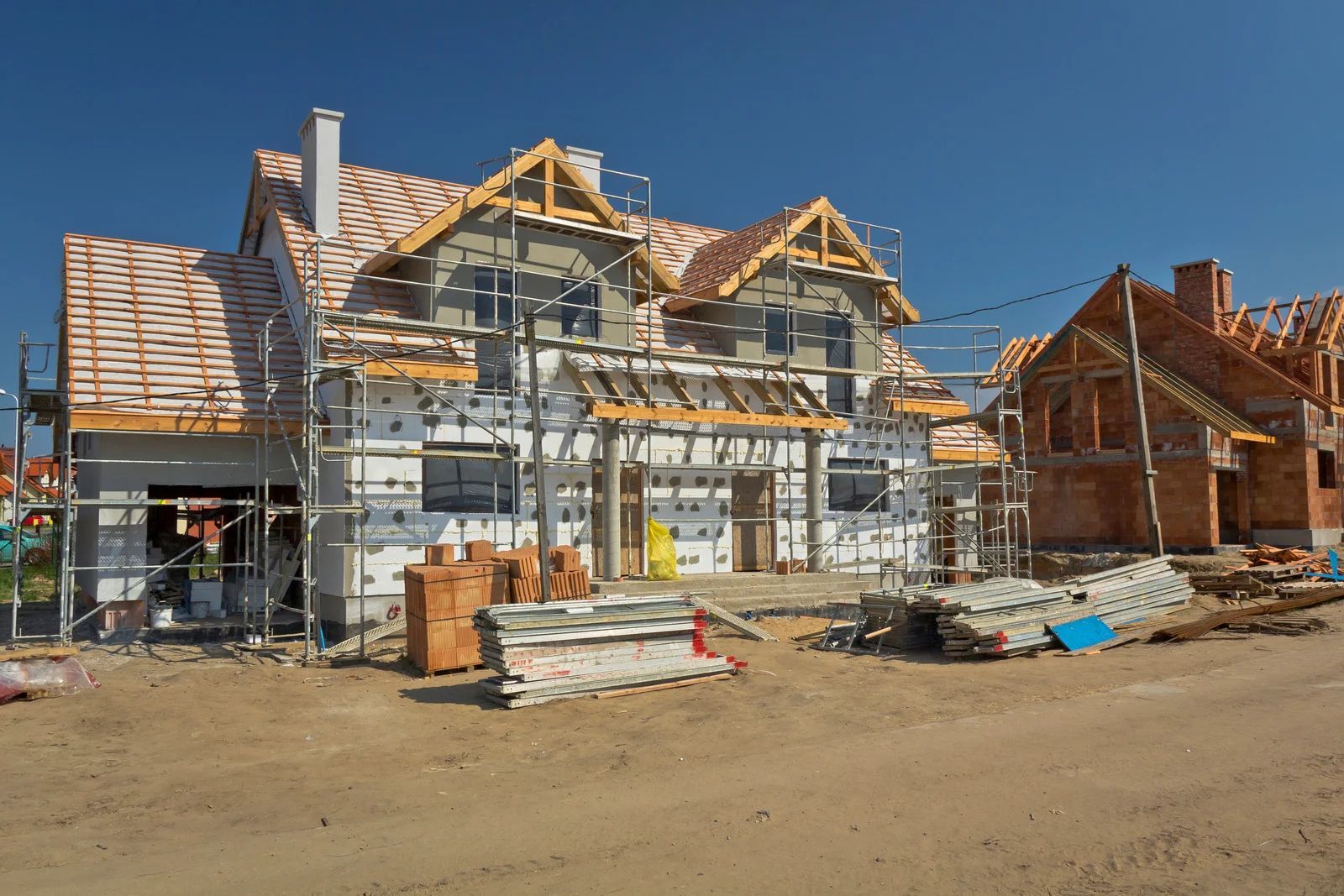 Houses under construction on a sunny day, with scaffolding and building materials.