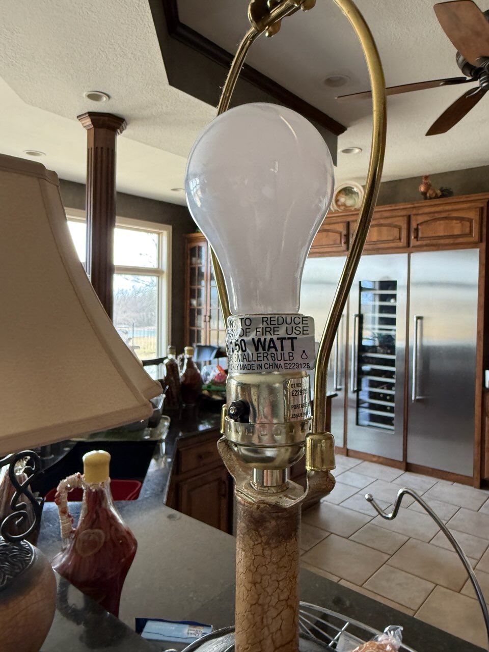 White light bulb on a cork stand in a kitchen beside a stainless steel refrigerator and window.