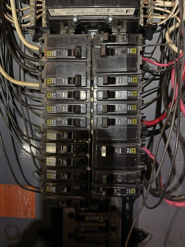 Electrical breaker panel with rows of switches and bundled black, yellow, and red wires.