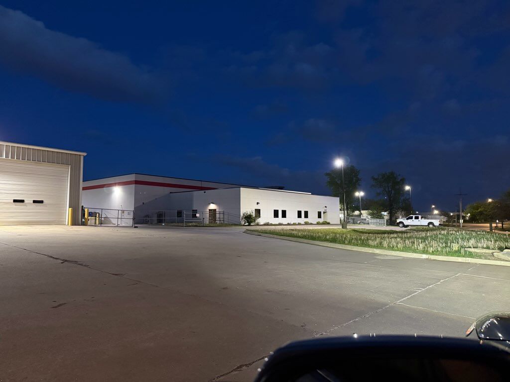 Quiet industrial parking lot at dusk with warehouse buildings and streetlights under a dark blue sky