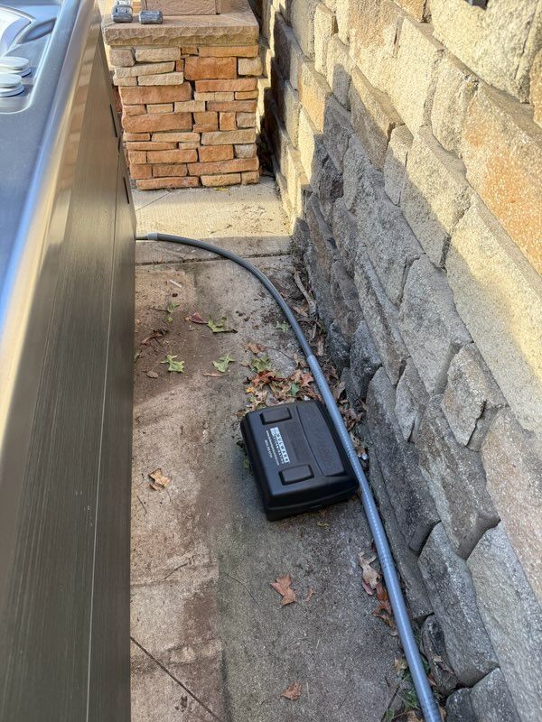 Narrow side yard with a black utility box and hose or cable along a stone wall beside a parked car