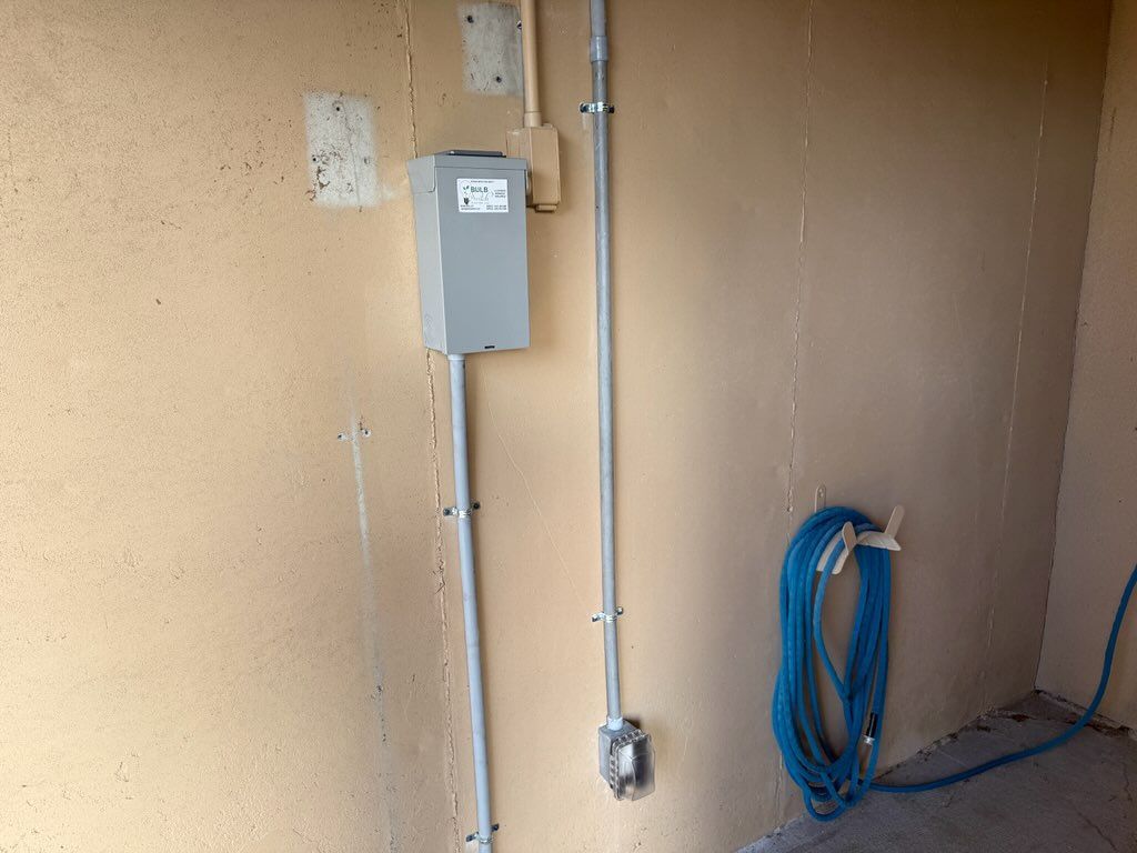 Electrical panel, conduit, and coiled blue cable on a beige wall in an unfinished room.