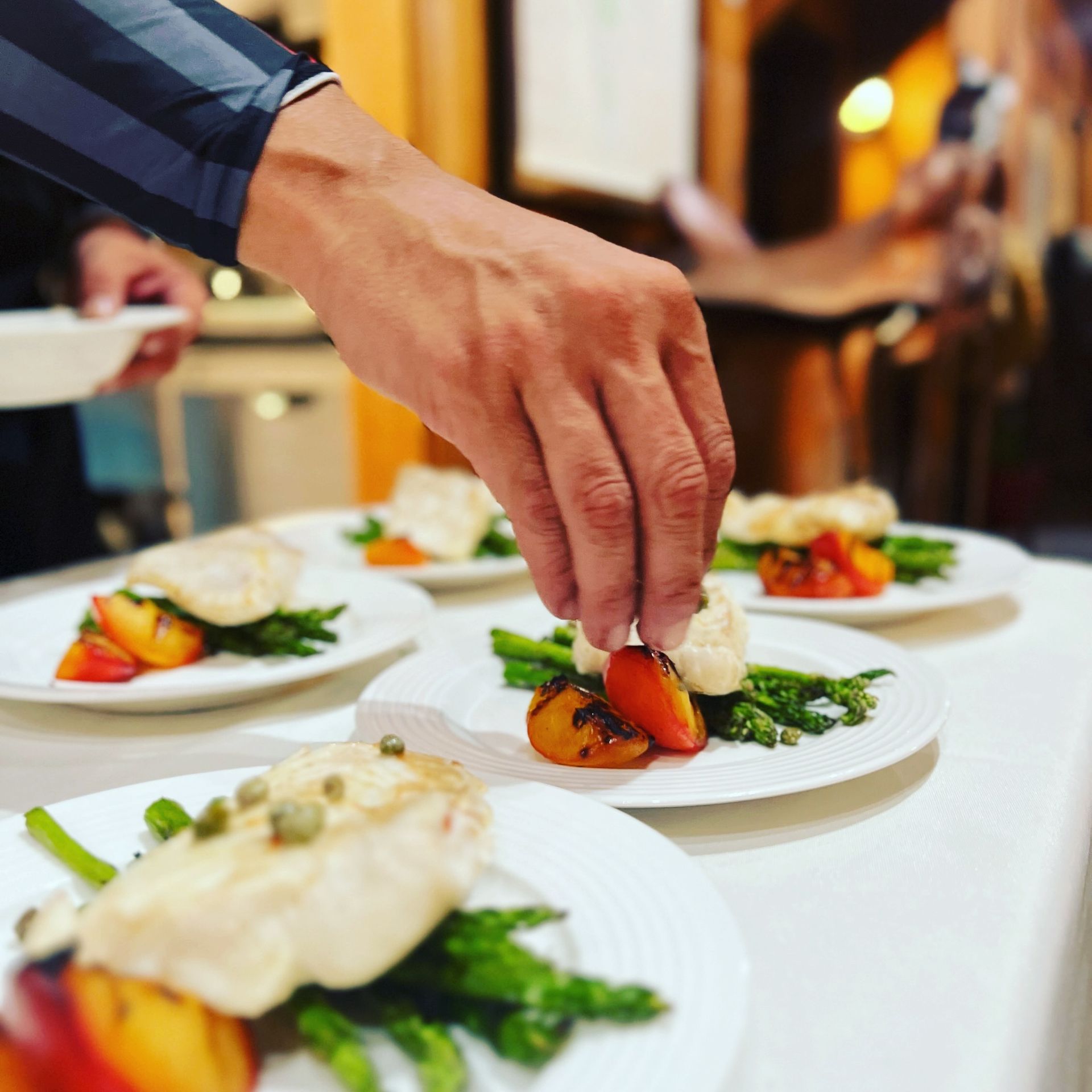 A person is putting a tomato on a plate of food