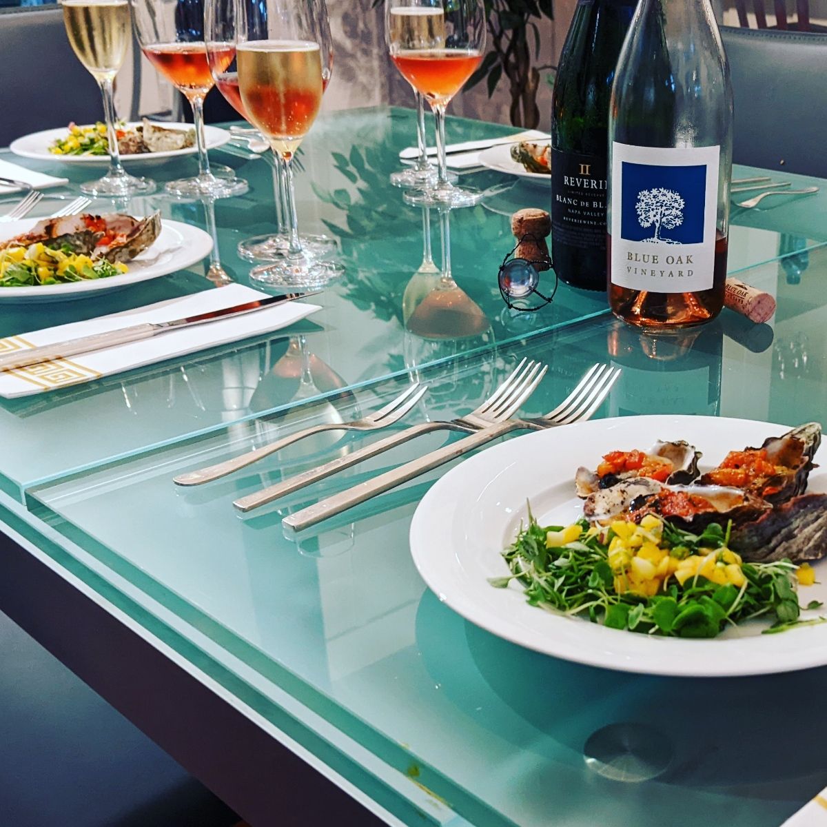 A glass table topped with plates of food and wine glasses