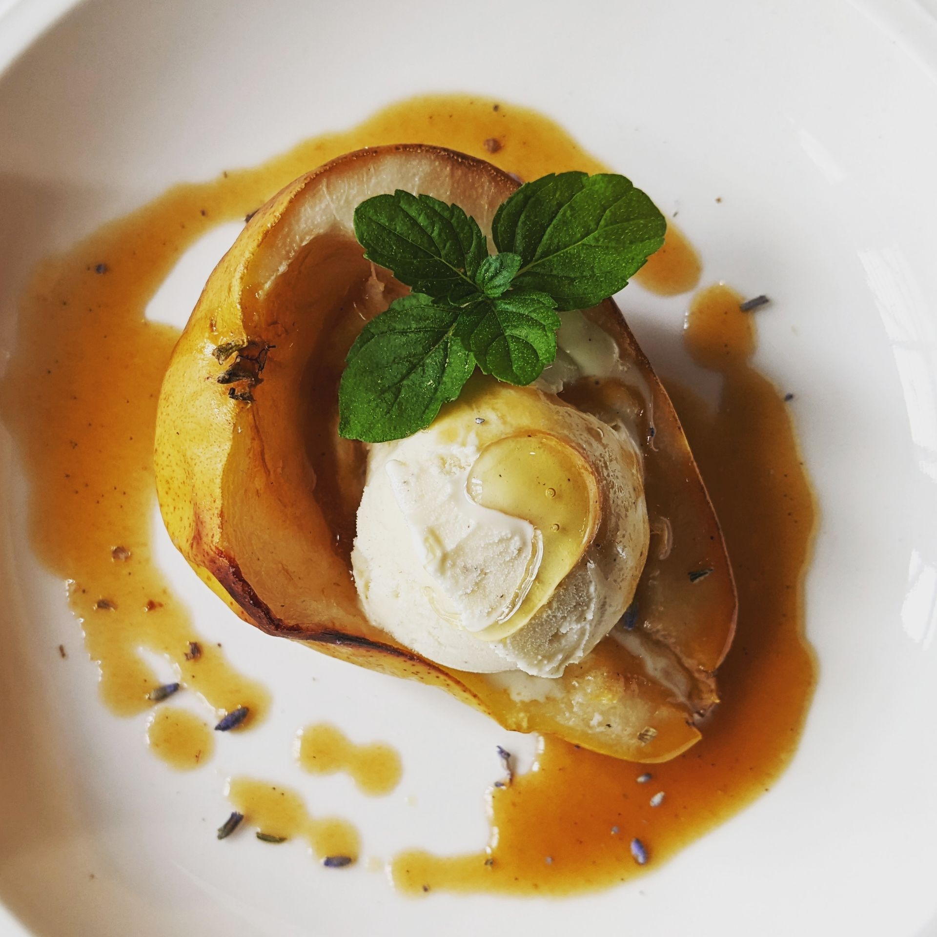 A white plate topped with a pear and ice cream