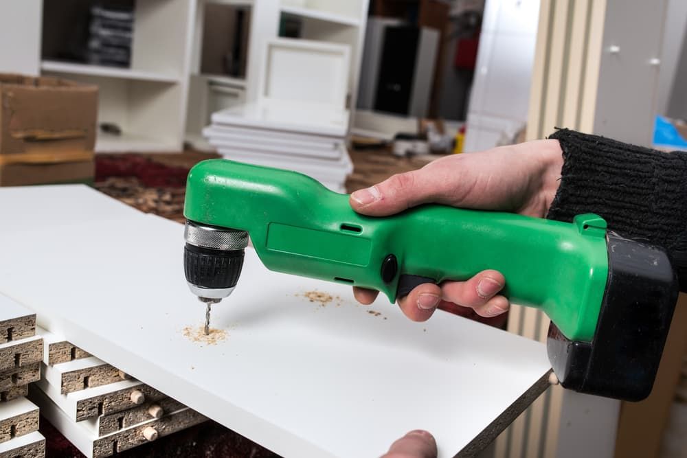 A Person Is Using a Green Drill to Drill a Hole in A Piece of Wood — Top End Joinery In Yarrawonga, NT