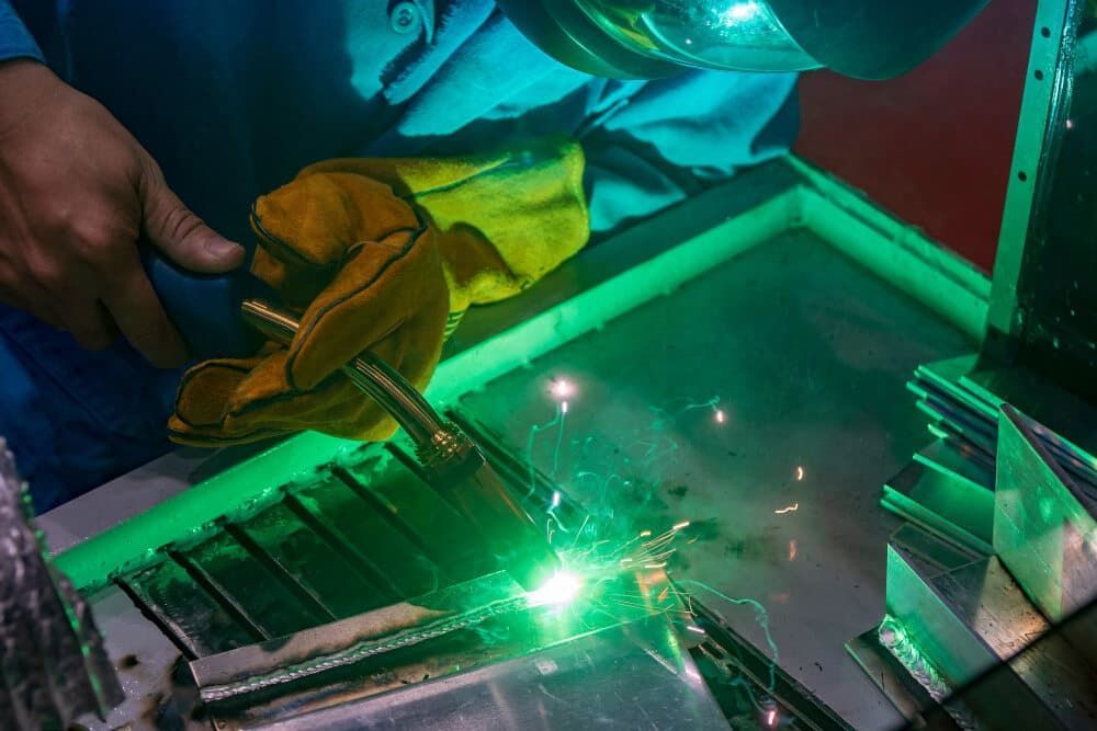A Man Is Welding a Piece of Metal with A Green Light — Top End Joinery In Yarrawonga, NT