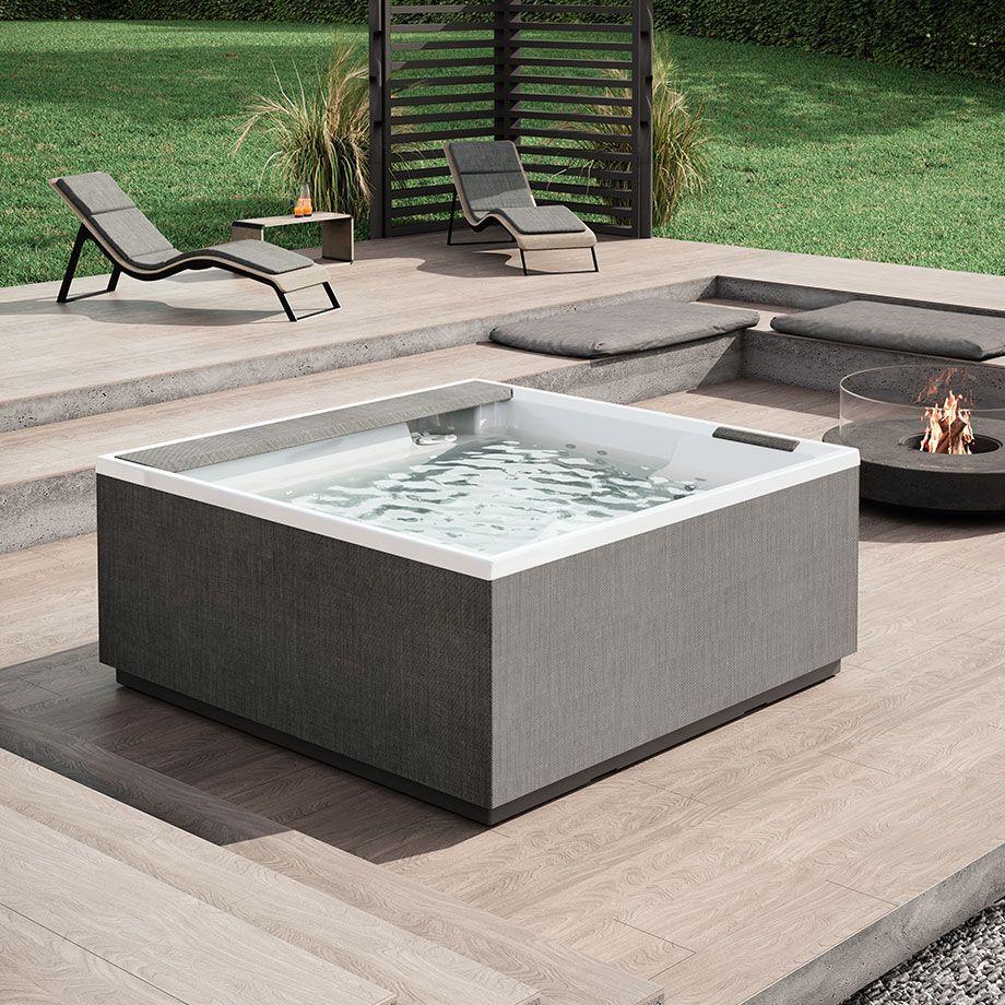 Una vasca idromassaggio quadrata è posizionata su una terrazza in legno accanto a un braciere.