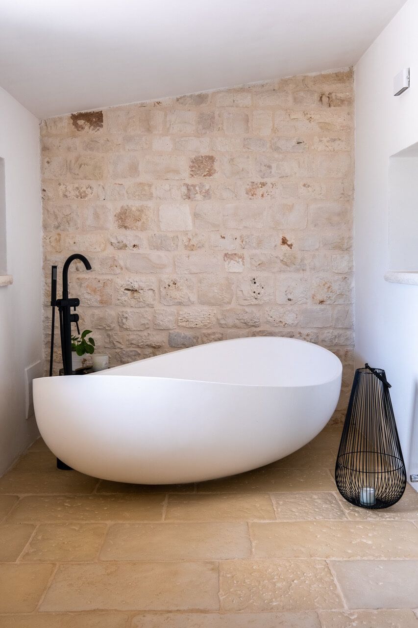 Un bagno con una grande vasca bianca e un muro in pietra.