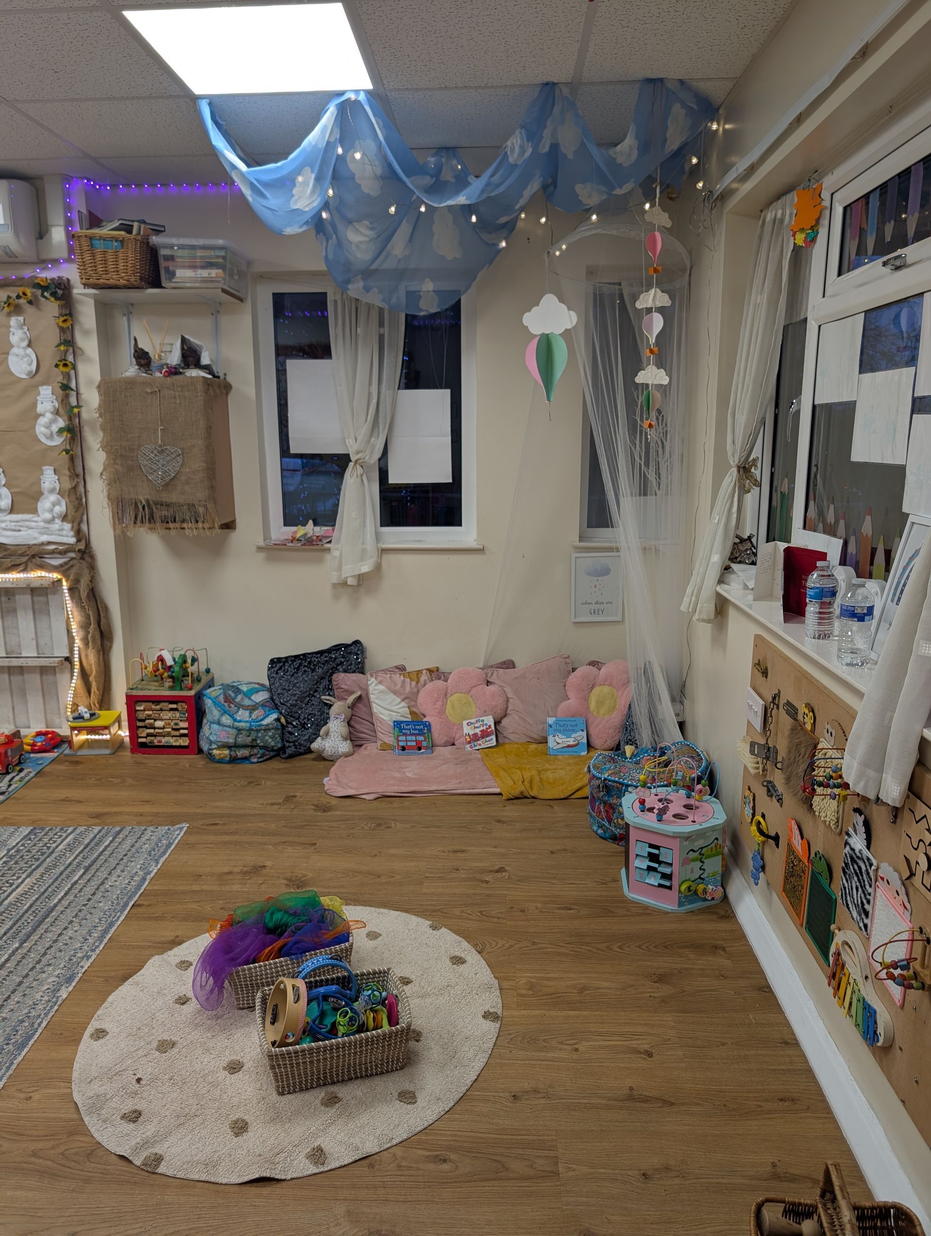 Decorated classroom corner with blue ceiling drapes, shelves, toys, and a rug on the floor