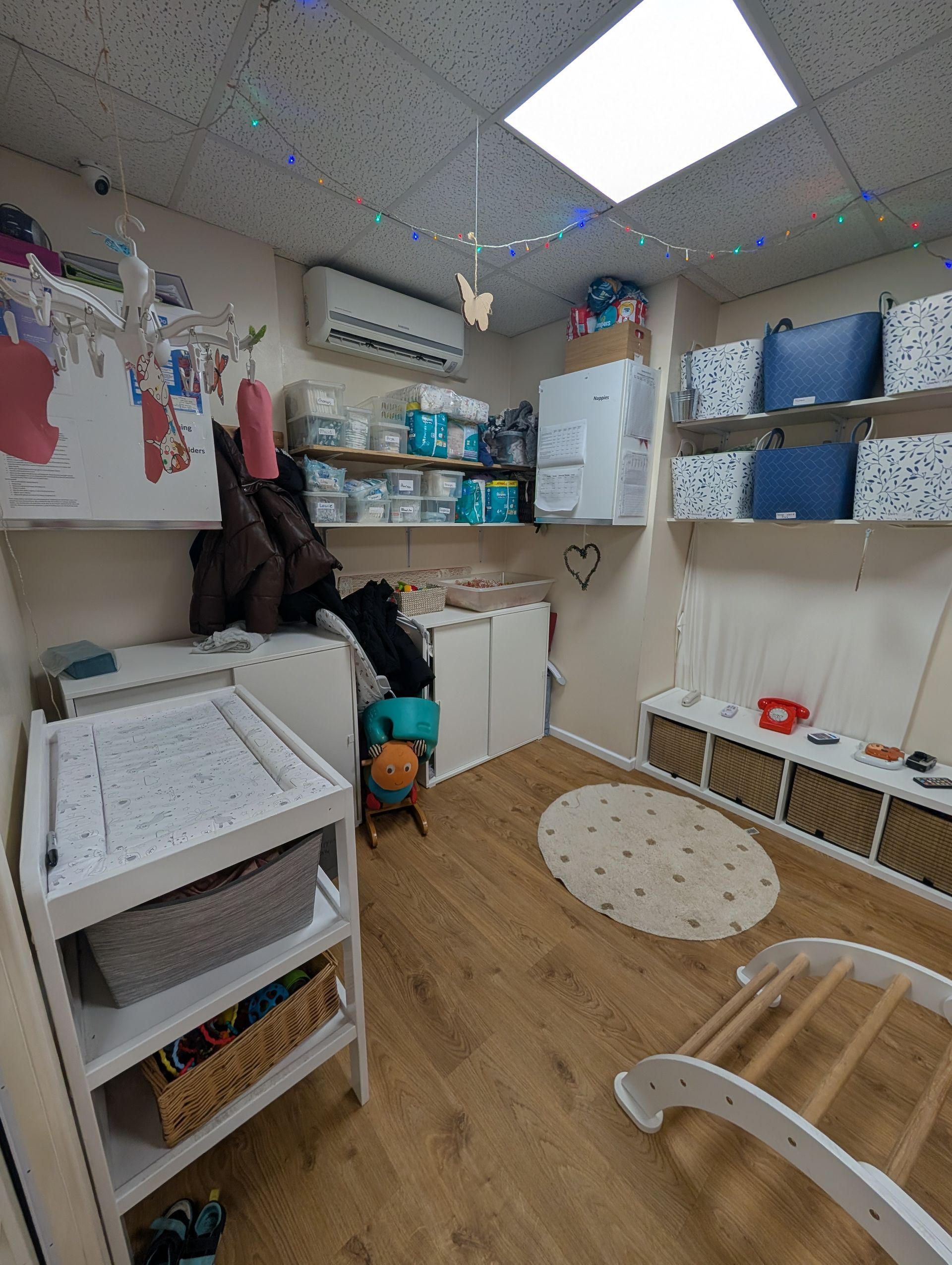 Small classroom or therapy room with a changing table, shelves, chairs, and colorful wall decorations.