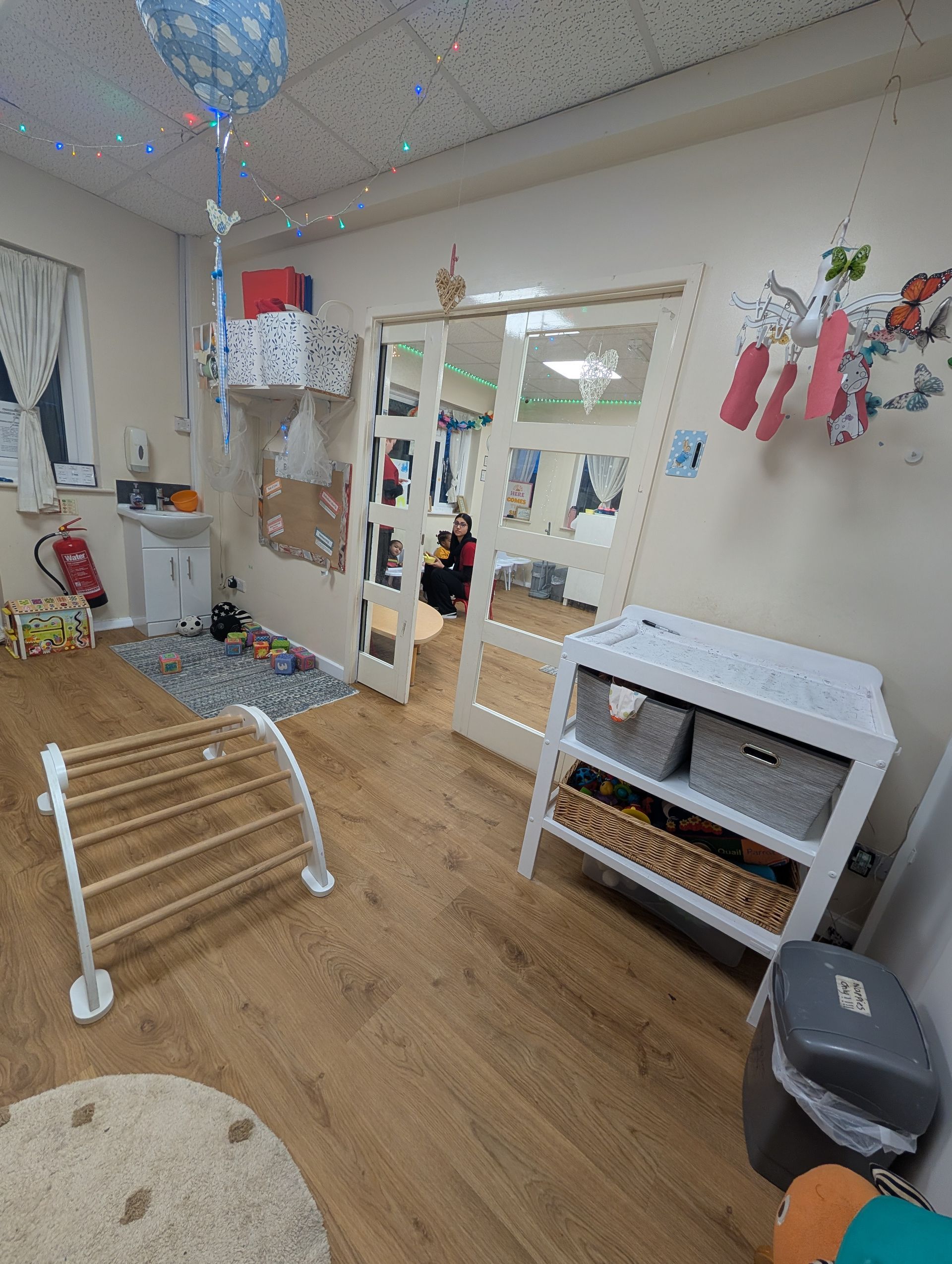Playroom with wood floor, toys, hanging decorations, and a white storage shelf by a glass door.
