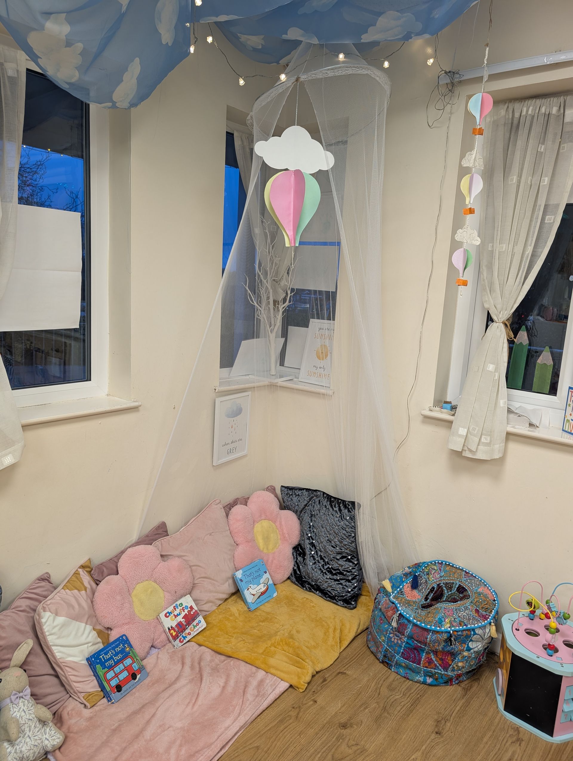 Cozy child’s corner with pink bedding, cushions, string lights, and curtains in a small bedroom nook