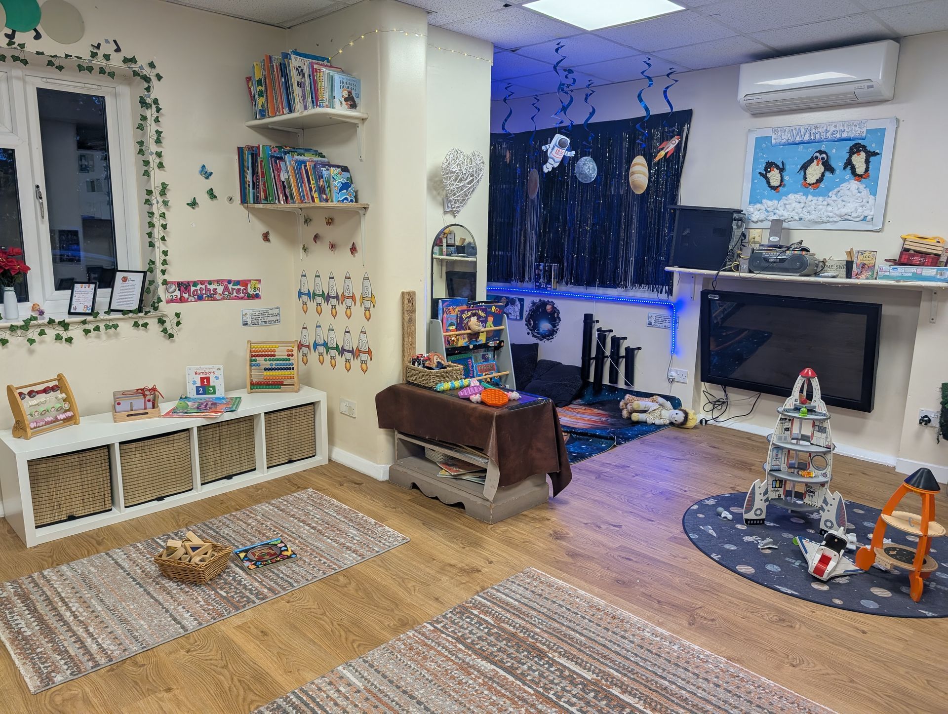 Colorful child’s playroom with rugs, toys, shelves, and a TV under a dark window curtain.