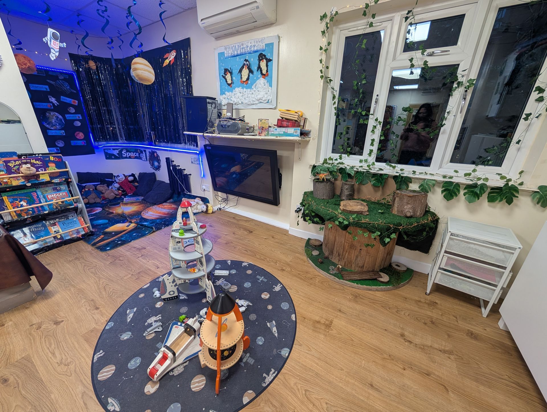 Playroom with toys on a rug, blue string lights, plants, and a window seating area