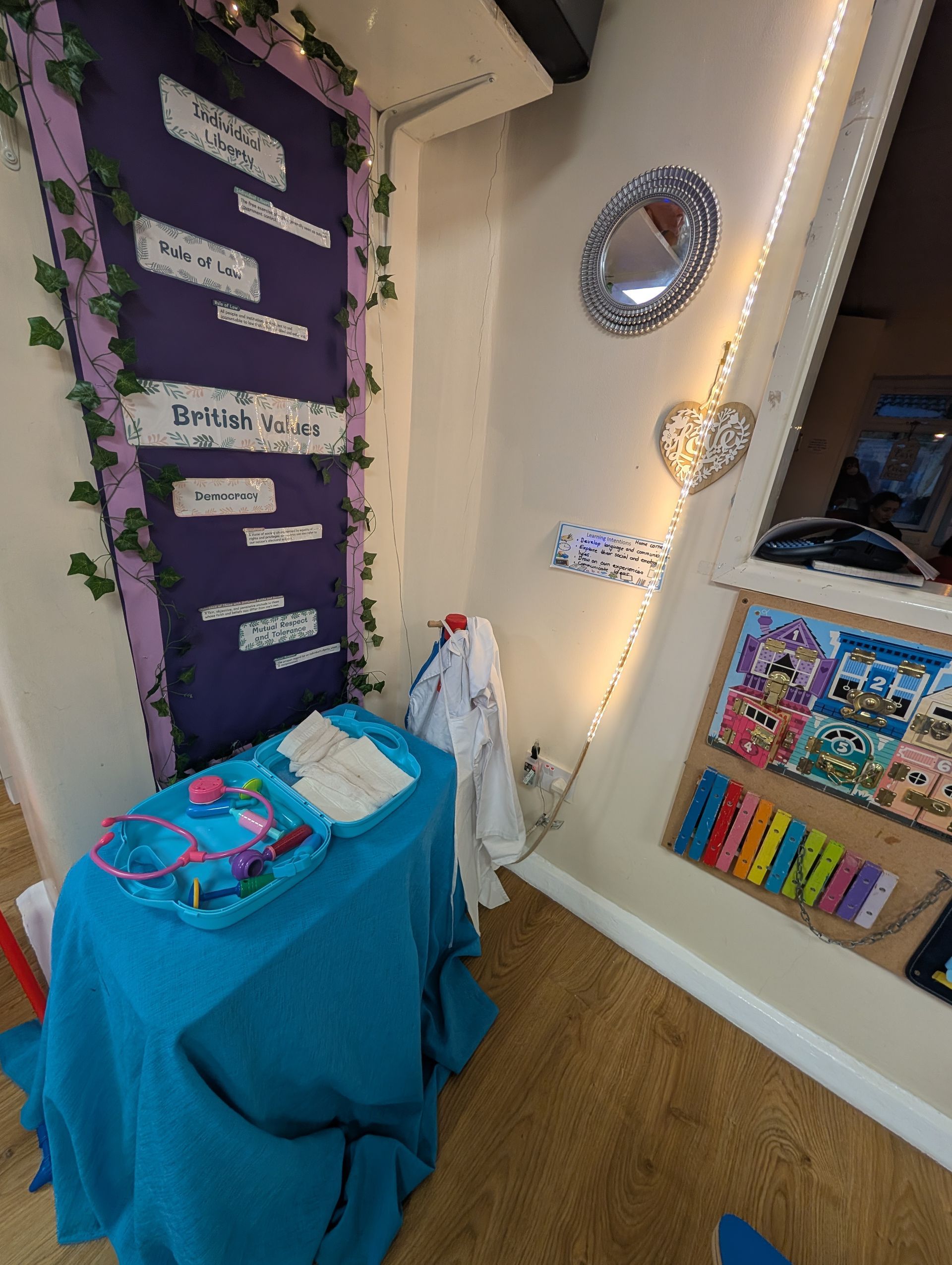Purple classroom display with a blue-covered table, fairy lights, and colorful wall decorations
