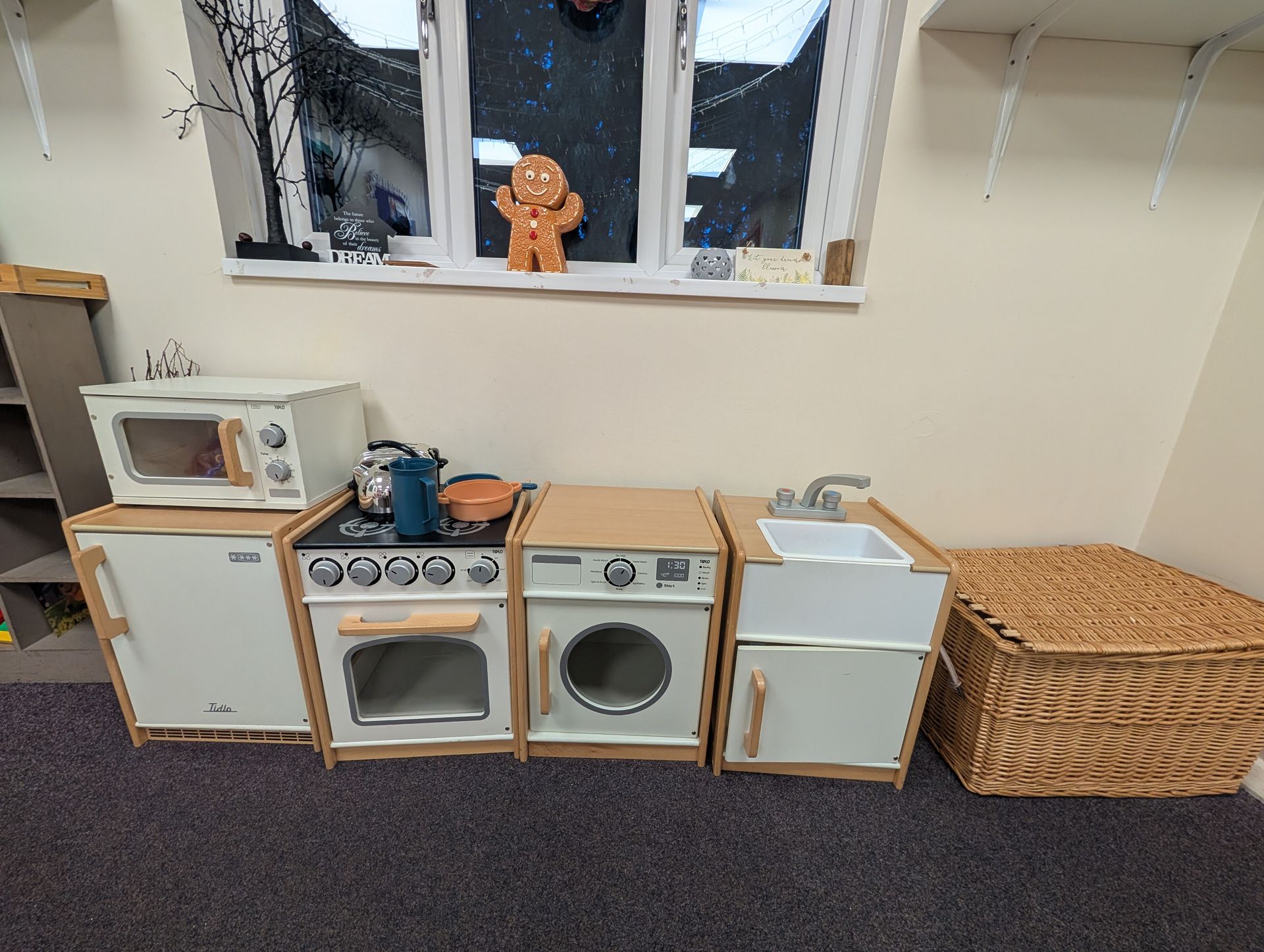 Miniature laundry room with toy washer, dryer, stove, microwave, and wicker basket on a shelf under a window