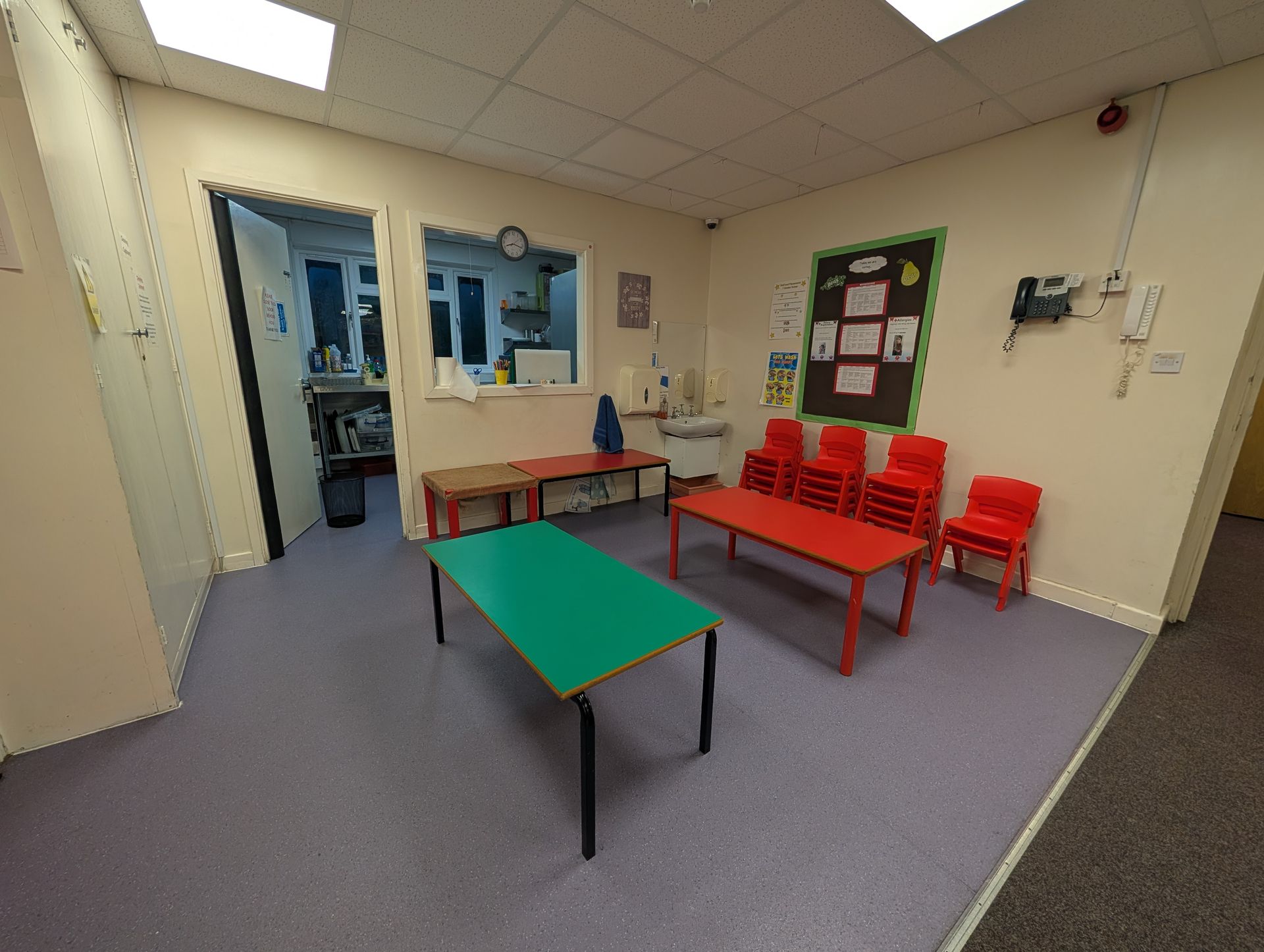 Small waiting room with red chairs, green table, bulletin board, and blue door window
