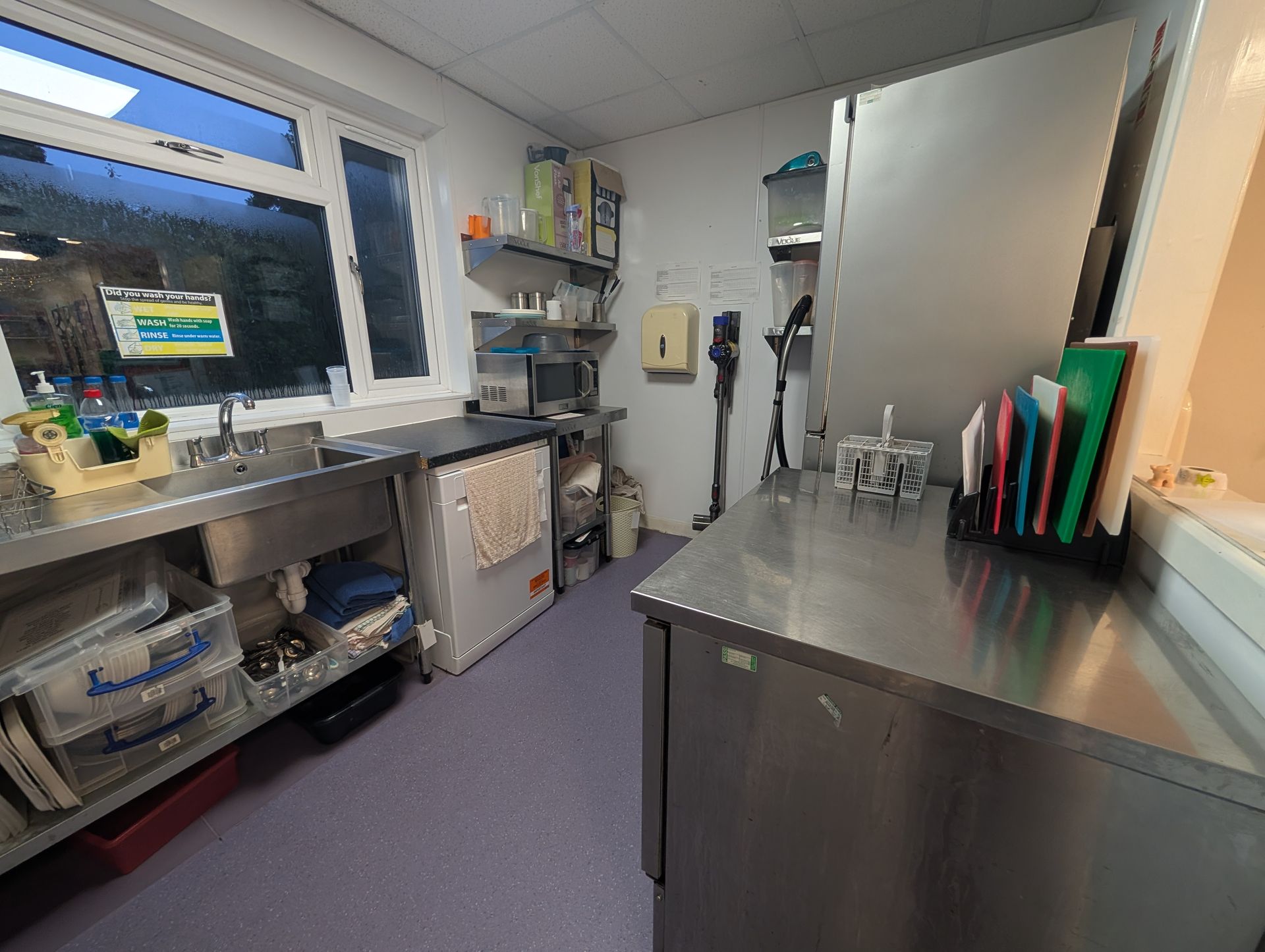 Compact stainless-steel laboratory workspace with sink, shelves, and equipment beside a window