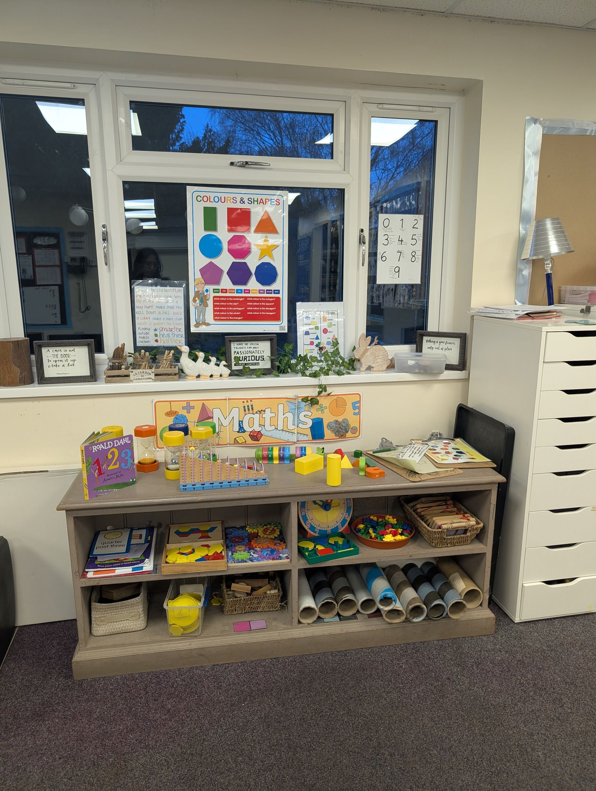Classroom sensory play shelf with colorful toys, bins, and learning posters under a window