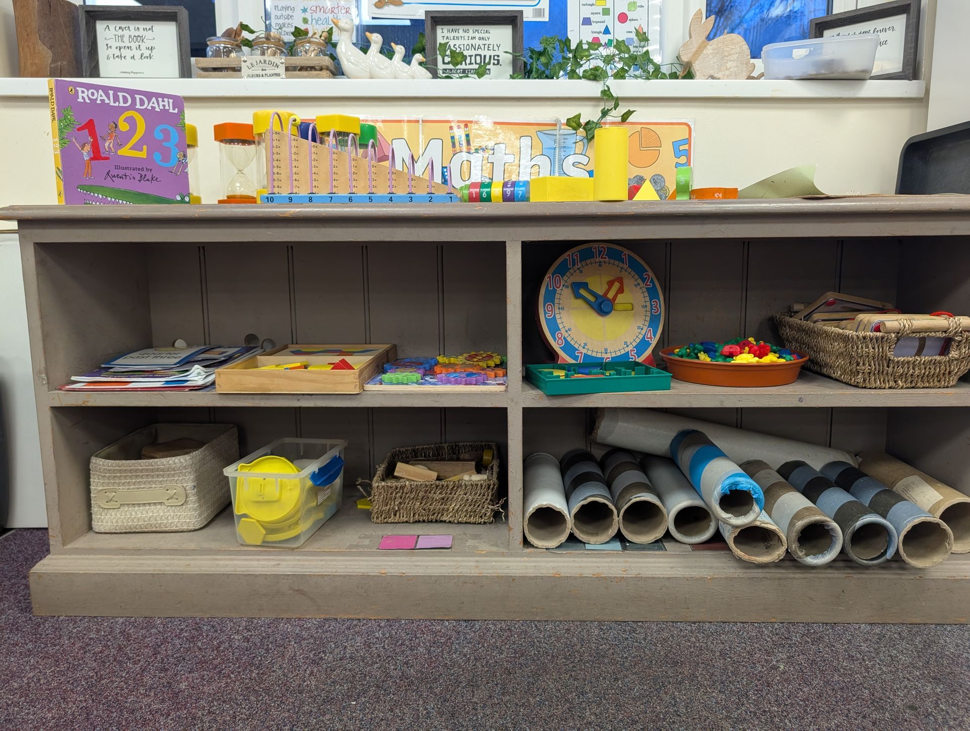 Classroom shelf with colorful bins, art supplies, and rolled paper tubes under a decorative “Welcome” sign
