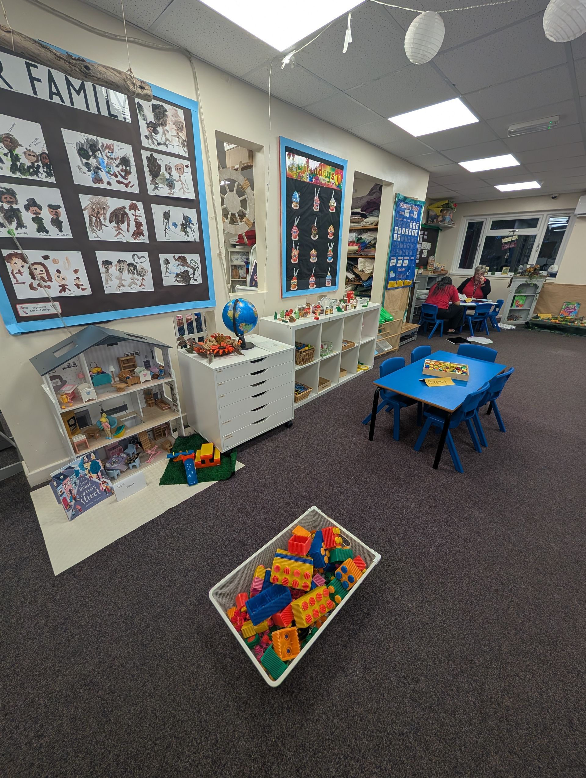Classroom with colorful learning stations, shelves, tables, and wall displays on a carpeted floor.