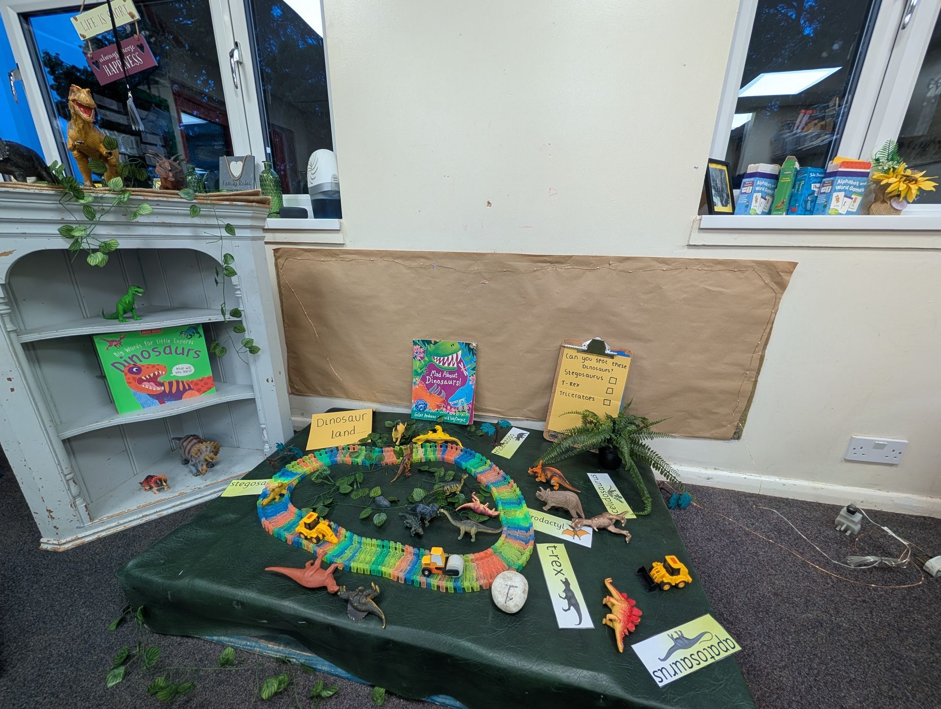 Children’s garden diorama with colorful plants, toy animals, and a small pond on a black mat in a classroom
