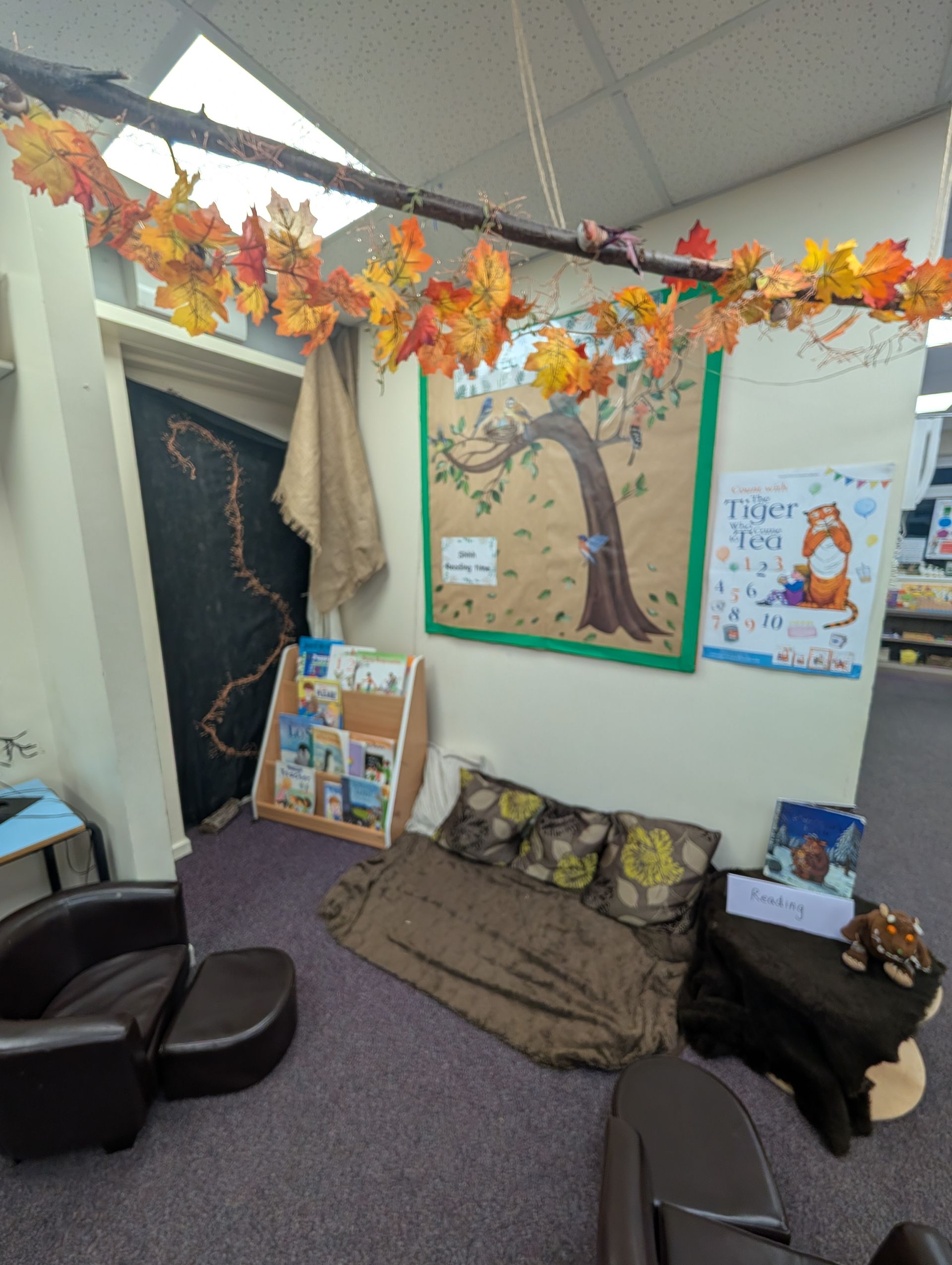 Cozy classroom reading nook with beanbags, leaf garland, tree mural, and autumn decorations
