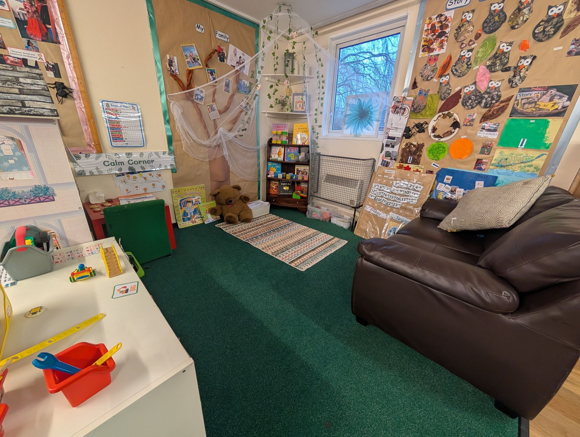 Cozy decorated room with a brown sofa, green carpet, and walls covered in colorful artwork and photos