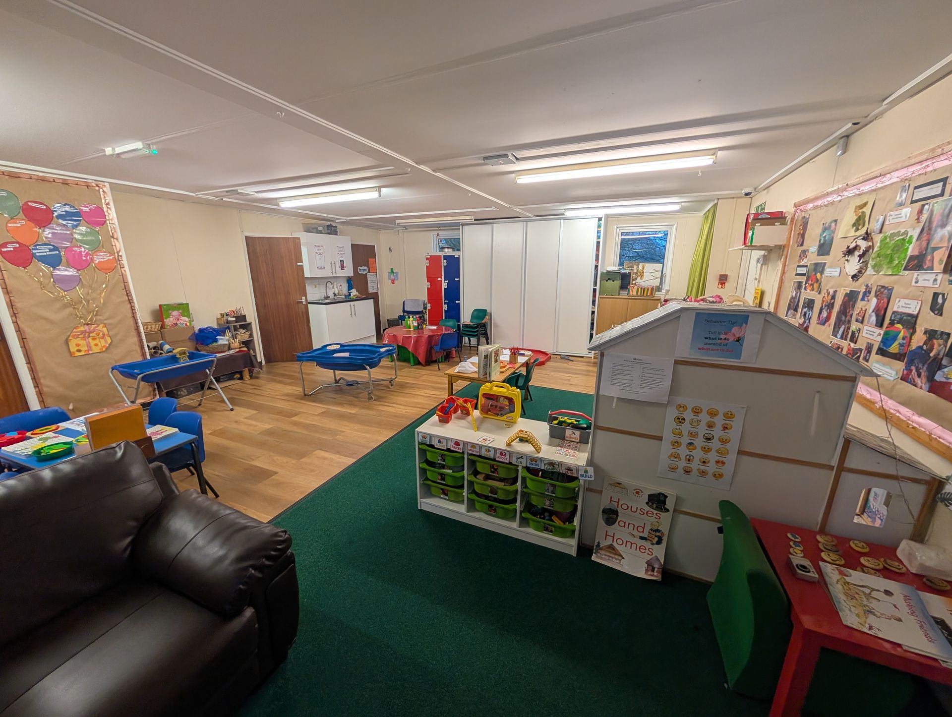 Childcare playroom with toys, colorful wall displays, and a couch on the left, viewed from a wide angle