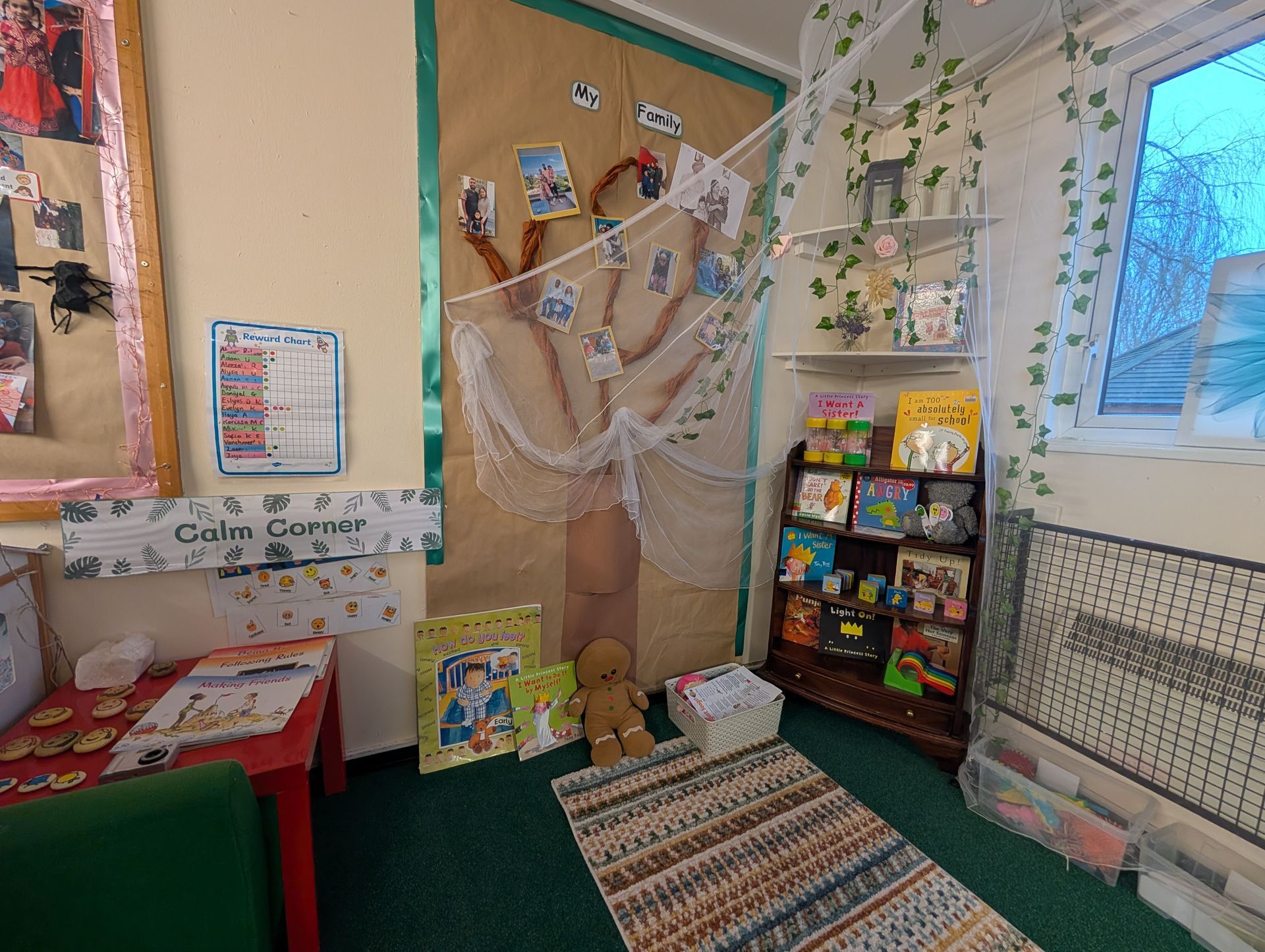 Cozy classroom reading corner with rug, books, bulletin board, cobweb decorations, and a window.