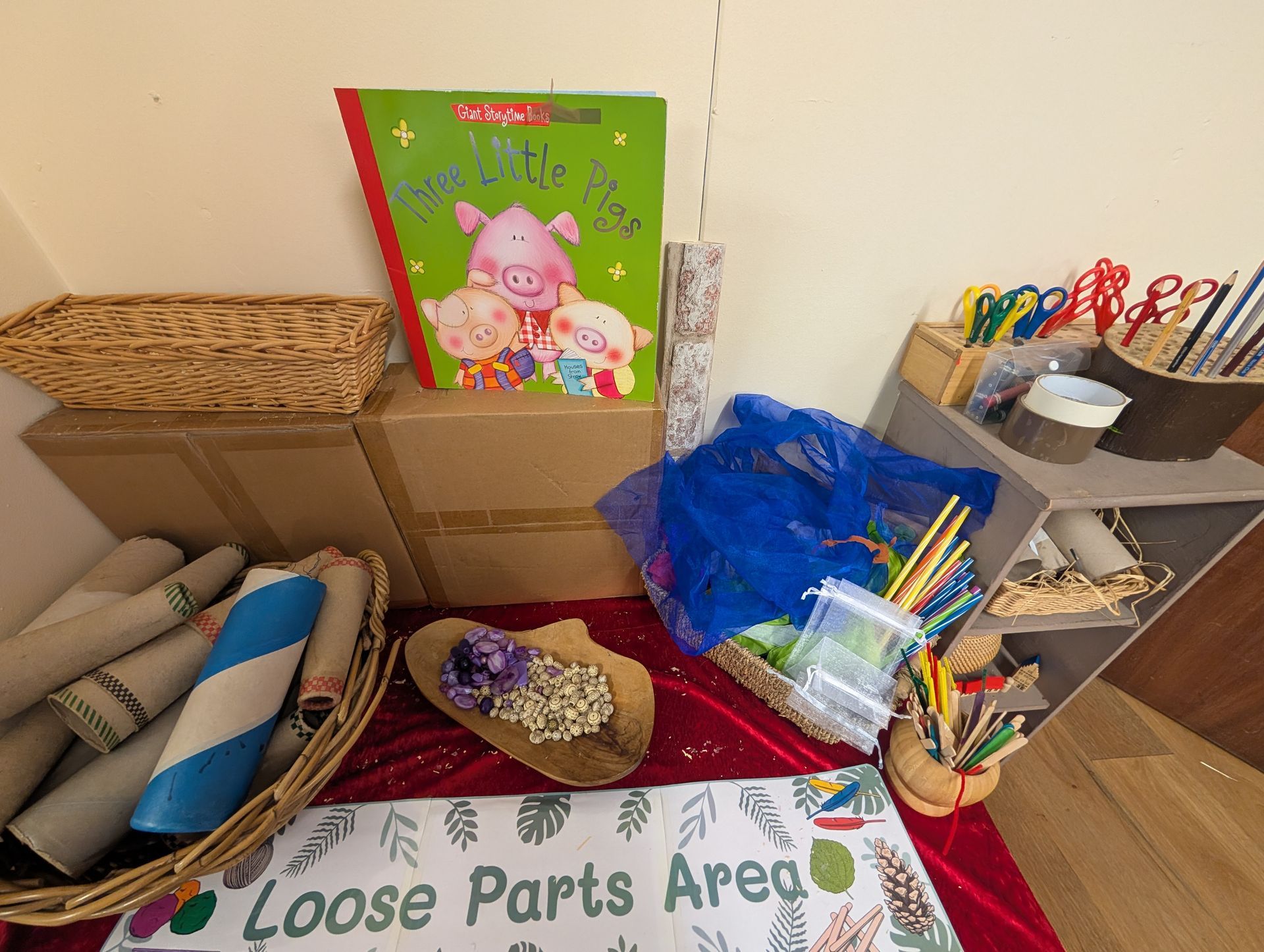 Loose parts area with baskets, cardboard tubes, crayons, and art supplies on a table