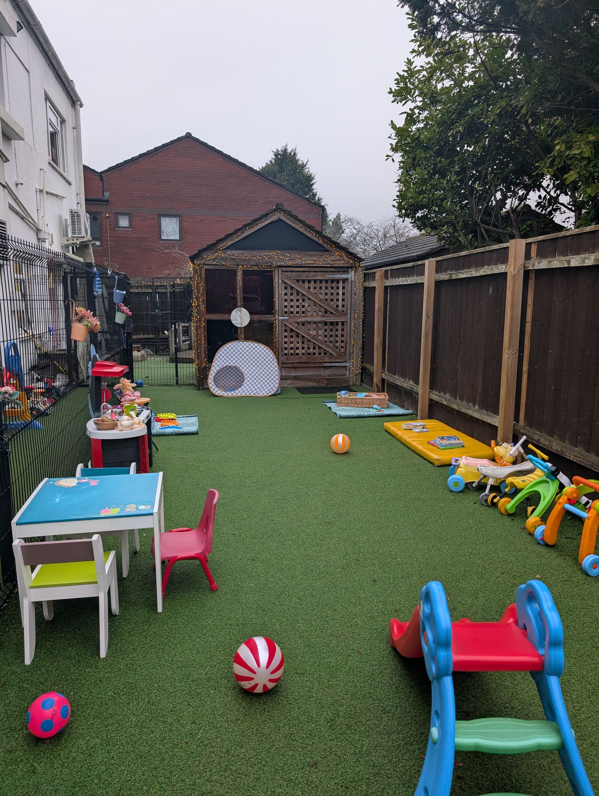 Backyard with artificial grass, kids’ toys, small table, playhouse, and fence on a rainy day