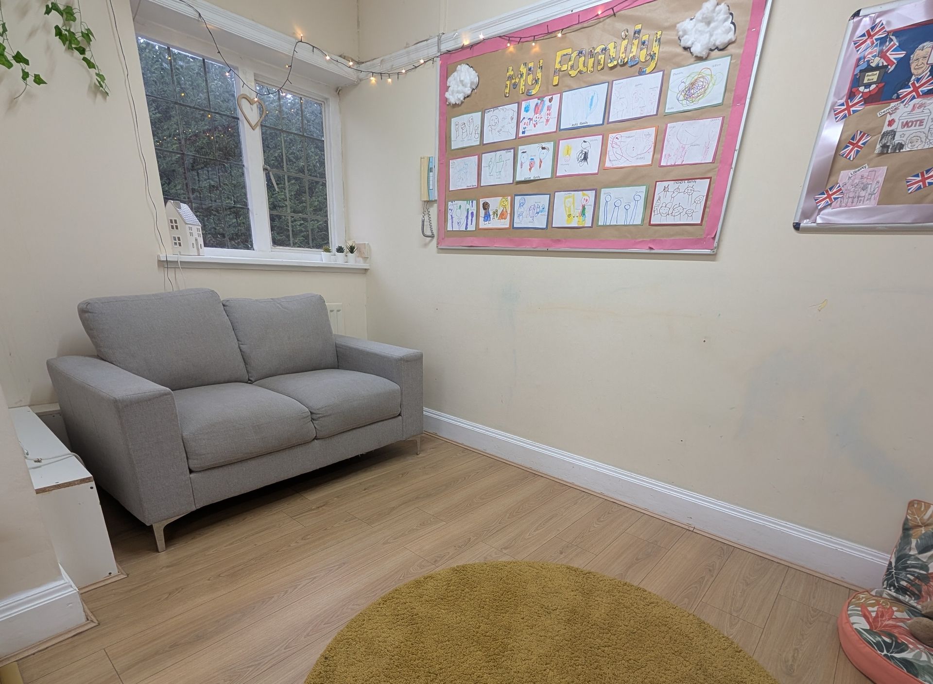 Small cozy room with a gray sofa, wall art, window, and a round rug on a wooden floor.