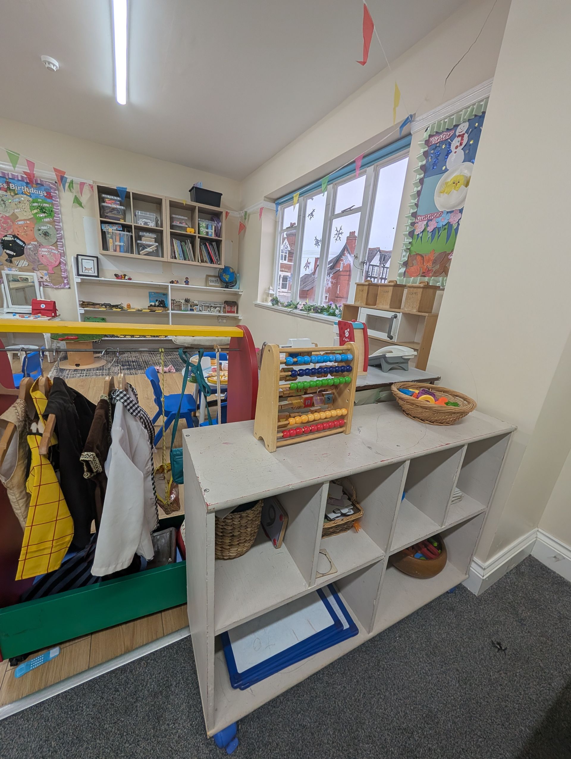 Classroom corner with cubbies, hanging coats, toy shelves, and a window by the sink area.