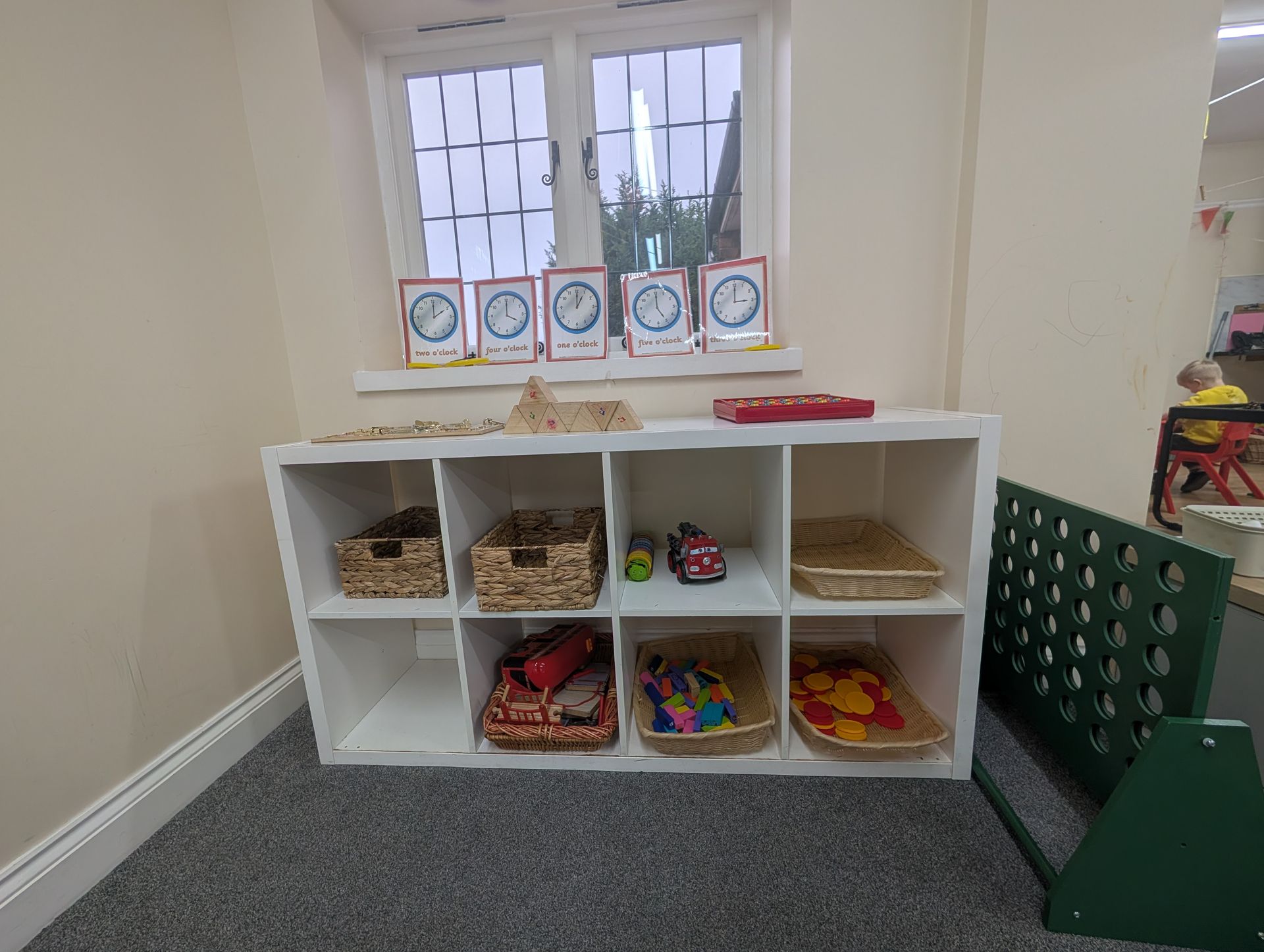 White cubby storage with baskets of toys and books beneath a window in a playroom.