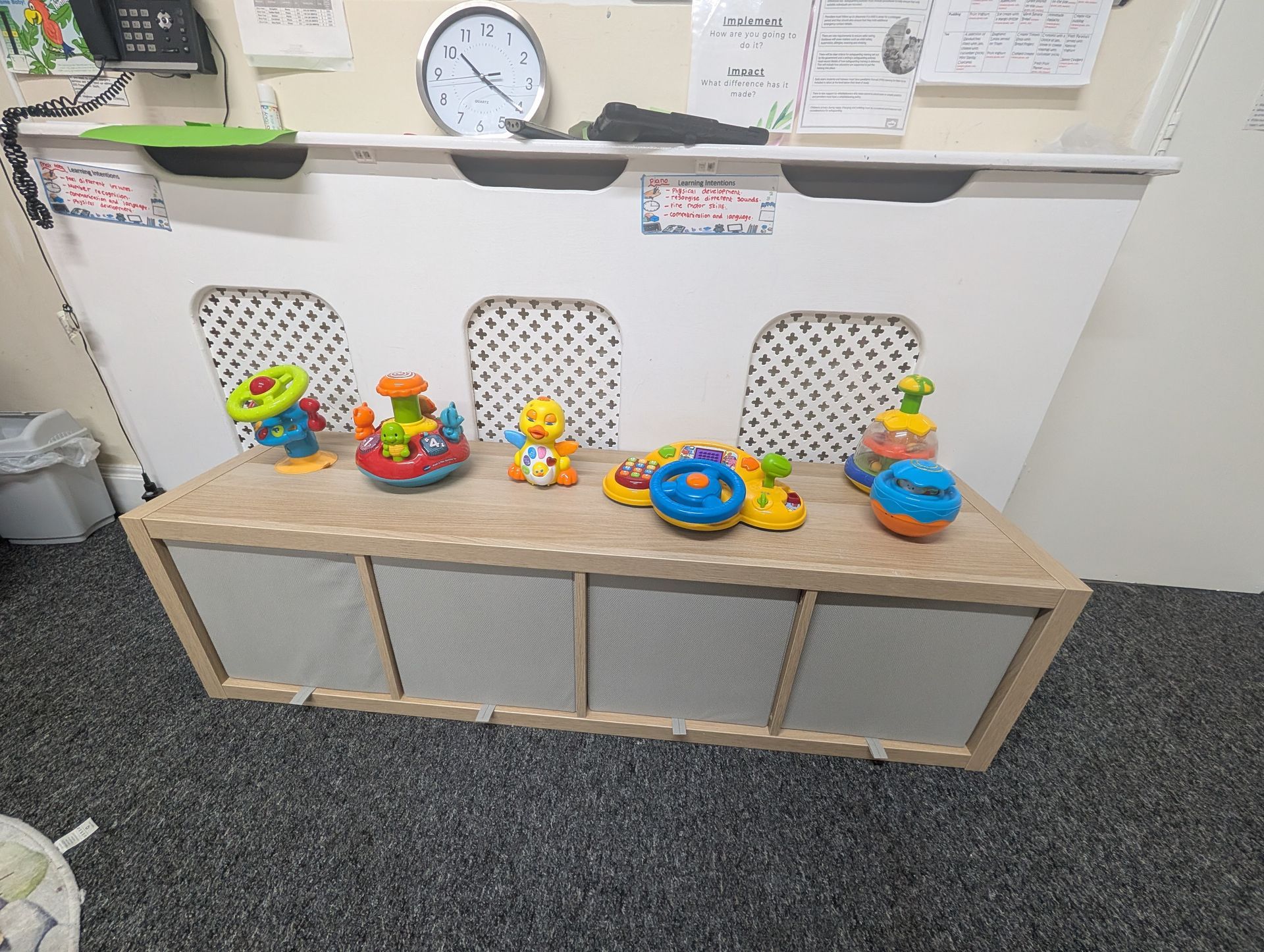Children’s play area with toys on a low shelf under wall art and a clock