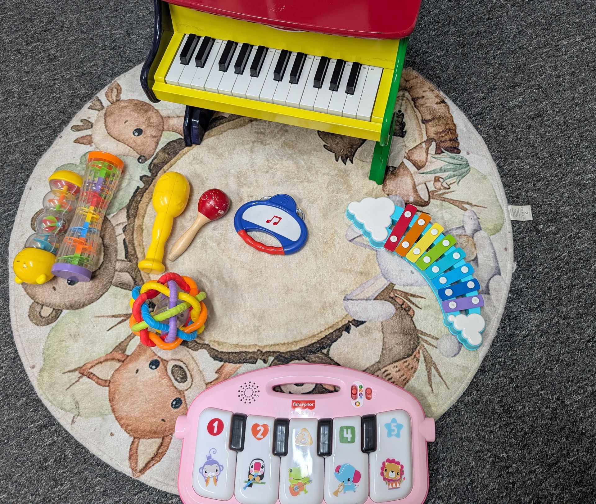 Colorful toys and a toy keyboard arranged on a round animal-patterned rug, with a pink toy laptop at the bottom.